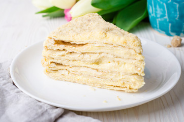 Slice of Napoleon cake with tulips on white vintage background. Selective focus