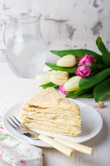 Slice of napoleon cake with tulips on white vintage background. Selective focus