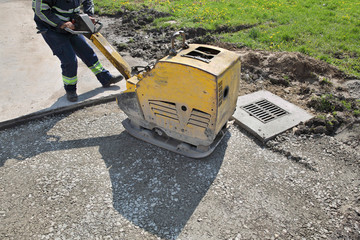 Worker use vibratory plate compactor at road construction site