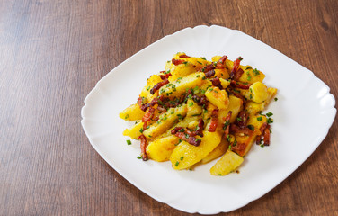 fried potatoes with bacon in a plate on wooden table