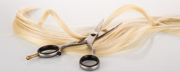 Hairdressing Scissors with a strand blond hair on a light background close-up