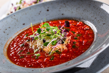 Soup. Tomato soup. Italian tomato soup. Mediterranean tomato soup. Italian cuicsine. Mediterranean food. Tomato soup with cheese and micro herb decoration. Serving of tomato soup on a spoon