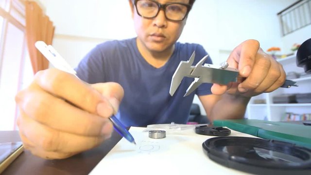 Engineer to hand sketch design part and measuring bearing by vernier caliper on work table 