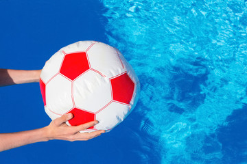 Fototapeta na wymiar Arms holding beach ball above swimming pool water