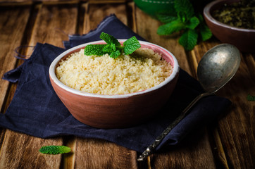 Couscous in clay bowl on wooden background. Selective focus. Toned image