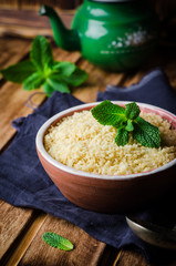 Boiled couscous in clay bowl on wooden background. Selective focus