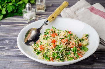Couscous salad with parsley and tomatoes on wooden background. Selective focus. Eastern cuisine