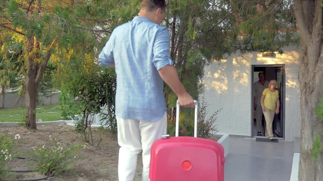 Happy grandparents meeting little grandson and his parents by the house. Mother and father rolling suitcases. After hugs and kisses they going indoors