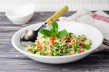 Couscous salad with parsley and tomatoes on wooden background. Selective focus. Eastern cuisine