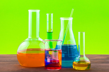 Different laboratory glassware with water and empty with reflection on green background