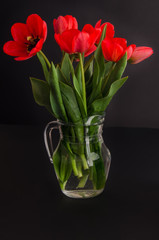 Bouquet of red tulips in a jar of glass on a black background