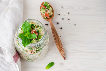 Couscous salad with parsley and tomatoes in jar  on white wooden background. Selective focus. Eastern cuisine