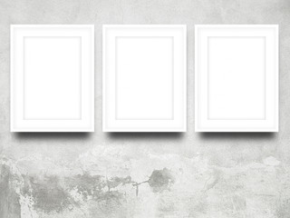 Close-up of three white blank picture frames on grey weathered concrete wall background