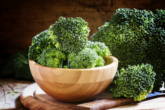 Fresh green broccoli in a wooden bowl on dark wooden background,