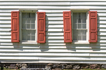 Two vintage windows with red shutters on white clapboard house