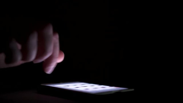 Person using phone in dark room with screen lighting scene.
