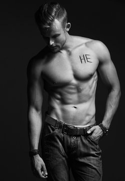 Handsome muscular male model with intense glance posing over grey background. Perfect body with the inscription "he" on his chest . Studio shot