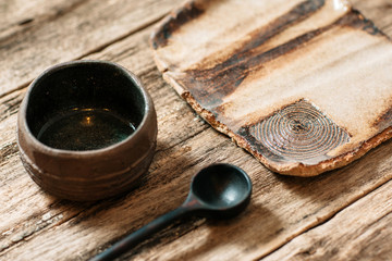 Obraz na płótnie Canvas Rustic handmade eco friendly pottery crockery set on wooden table. Creative brown ceramics with nature pattern. Empty clay plate, wooden spoon and ceramic bowl on old wooden background