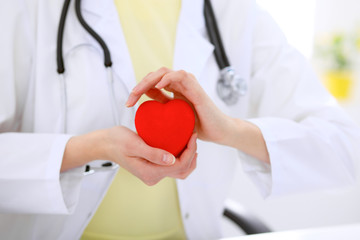 Female doctor with stethoscope holding heart.  Patients couple sitting in the background