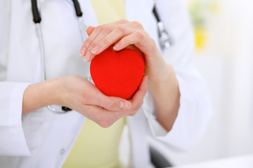 Female doctor with stethoscope holding heart.  Patients couple sitting in the background