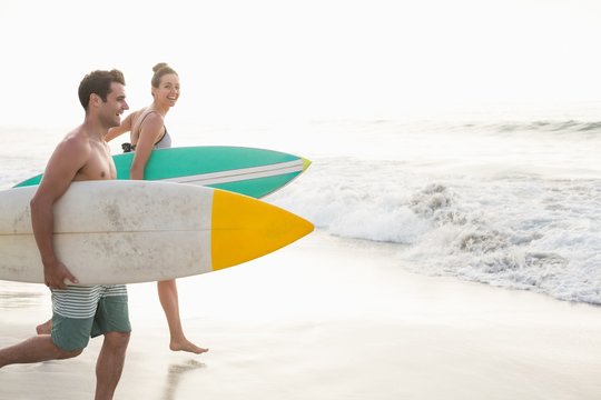 Couple with surfboard running on the beach - Powered by Adobe