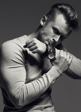 Advertising wrist watch concept. Beautiful (handsome) muscular male model with perfect body in grey jumper. He bites and unfastens the bracelet from the clock. Street style. Black and white 