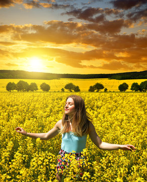 Young happy woman on blooming rapeseed field at sunset
