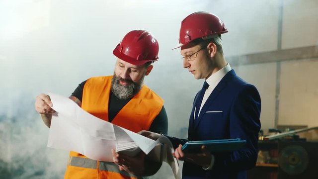 Intelligent engineering and brutal bearded construction worker studying drawings. enjoy Pad