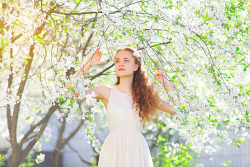 Fototapeta na wymiar Beautiful young girl with curly hair in spring flowering garden