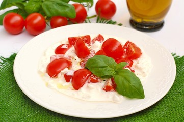 Salad from cherry tomatoes and cottage cheese with basil and olive oil