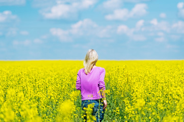 The young blonde in jeans walks on the rape field.