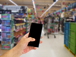 Man hand holding smart phone over blurred shopping center or super market background.