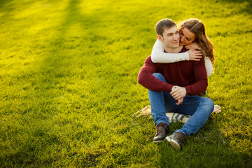Fototapeta premium Young couple spend a weekend or holiday in park or pine forest. Against backdrop of mist or fog. Family values, spending time together, youth. Hug and kiss each other on grass. Solid sweaters