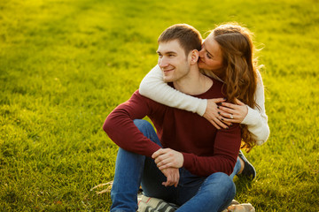 Young couple spend a weekend or holiday in park or pine forest. Against backdrop of mist or fog. Family values, spending time together, youth. Hug and kiss each other on grass. Solid sweaters
