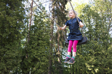 Little child blond girl having fun on a swing outdoor. Summer playground. Girl swinging high 