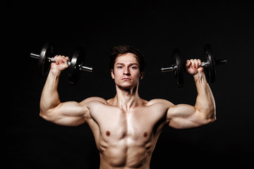 Fototapeta na wymiar Handsome athletic man with dumbbells confidently looking forward. Strong bodybuilder with six pack, perfect abs, shoulders, biceps, triceps and chest. Great fitness body. Ideal for commercial 