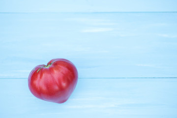Tomato in the shape of a heart on a blue wooden background.