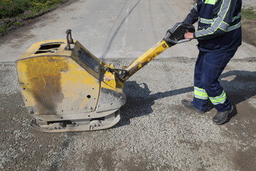Worker use vibratory plate compactor at road construction site - obrazy, fototapety, plakaty