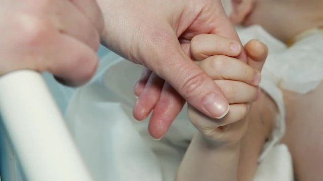 Close up of a young mother and sick child holding hands for comfort in a hospital bed 