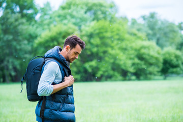Fototapeta premium Travel. Young man with a bag on green nature background thinking and look down.