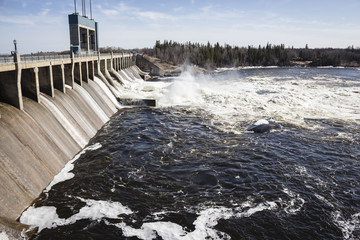 horizontal image of a large hydro dam with water churning aggressively over the turbines in the...