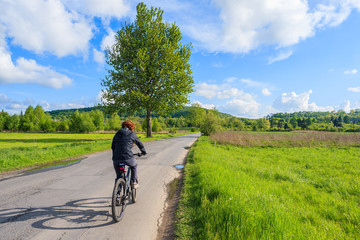 Obraz premium Young woman riding a bike on road along rural landscape near Krakow, Poland