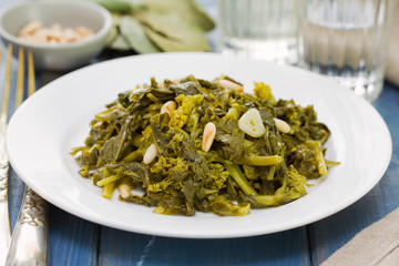 boiled turnip greens with nuts and garlic on white plate and glass of wine on blue wooden background