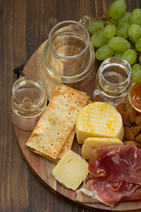prosciutto with cheese, cookies, grapes and white wine on brown wooden background