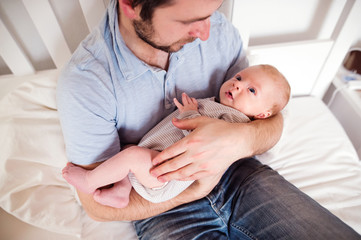 Young father holding his newborn baby son, home bedroom