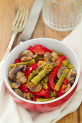 fried asparagus with vegetables in red bowl on brown wooden background