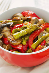 fried asparagus with vegetables in red bowl on white wooden background