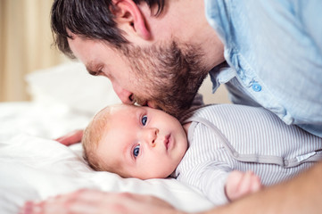 Baby boy lying on bed, held by his father