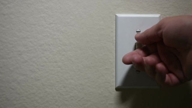 A hand turns off and turns on a light switch