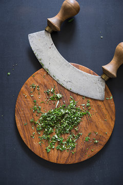 Italian traditional old mezzaluna knife and chopped herbs on cutting board